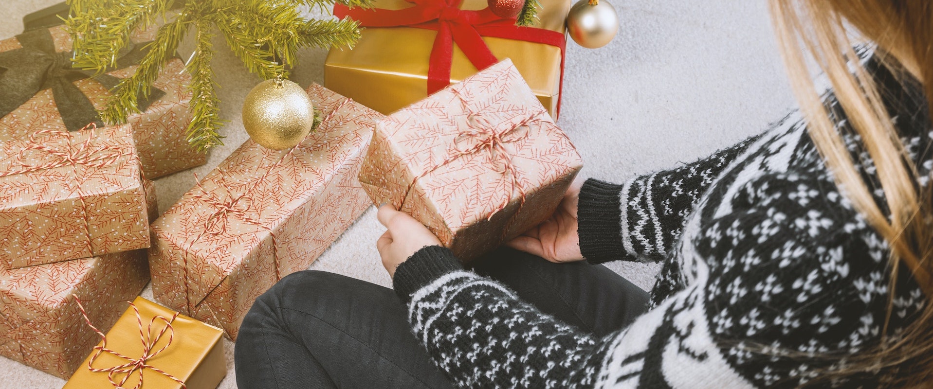 Eine Frau hebt ein verpacktes Geschenk von einem Geschänkehaufen hoch