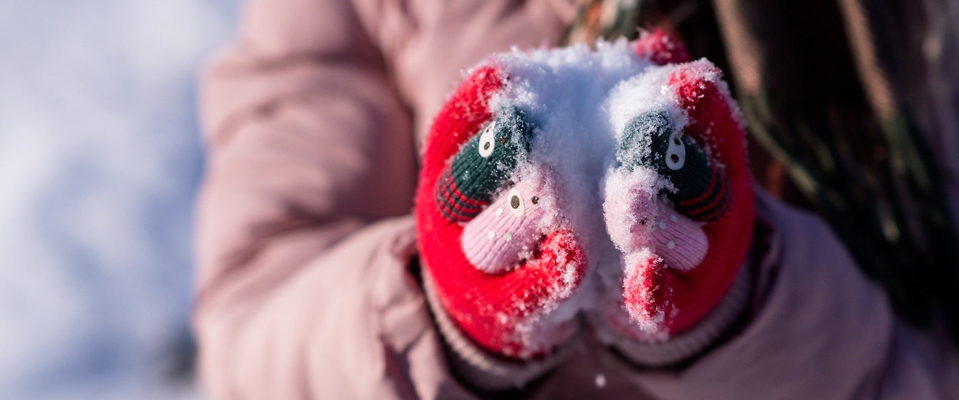 Eine Frau hält Schnee in ihren Händen mit angezogenen Handwärmern